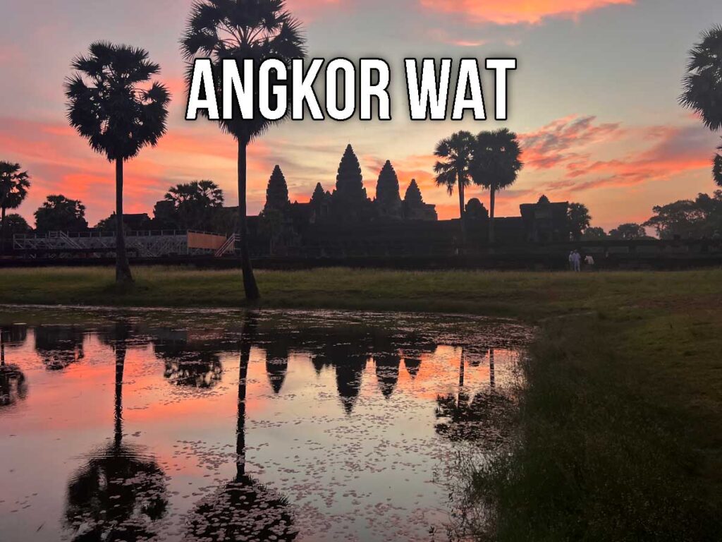 View of Angkor Wat silhouetted against a vivid pink and orange sunrise, with palm trees and temple towers reflected in a still pond in the foreground.