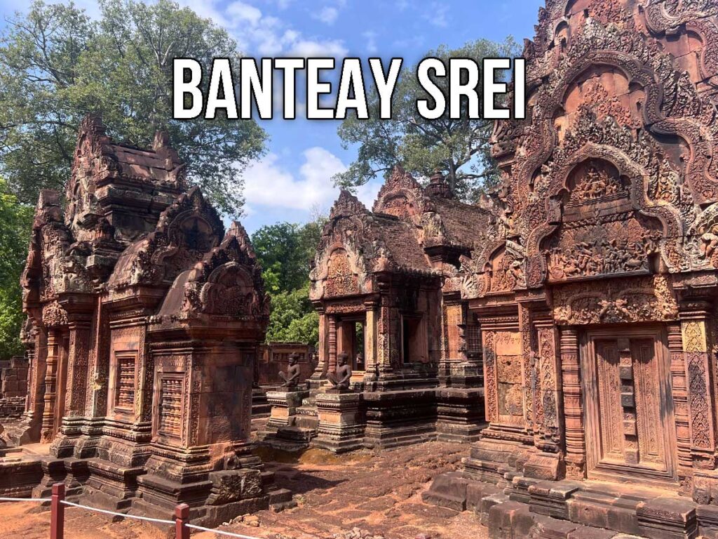 Intricately carved red sandstone towers and doorways at Banteay Srei, showcasing detailed Hindu mythological scenes under a clear blue sky.