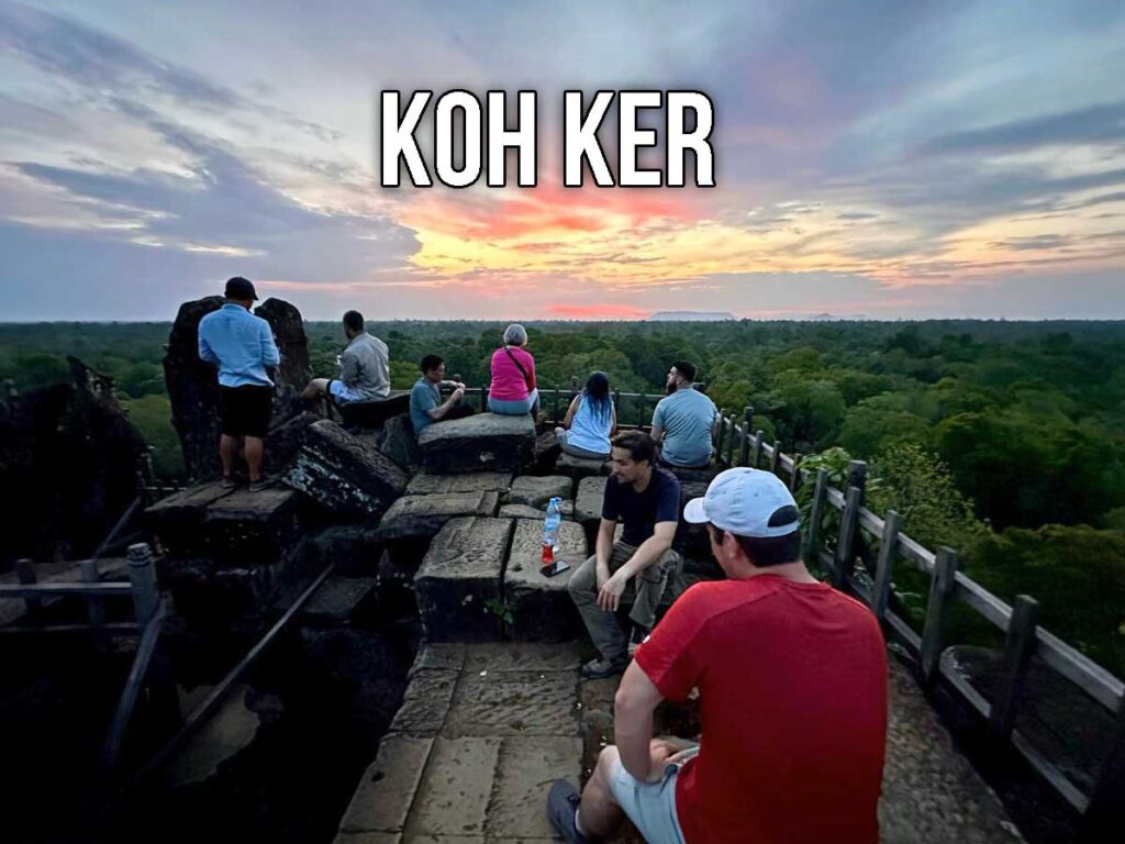 Tour group sitting atop the Prang temple at Koh Ker, looking out over the jungle canopy at sunset with a colorful sky in the background.