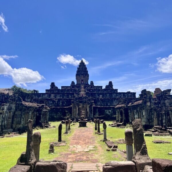 Front view of Bakong Temple in Cambodia showing the central pyramid sanctuary, ancient stone causeway, ruined galleries, and bright blue sky above the Khmer temple complex near Siem Reap.