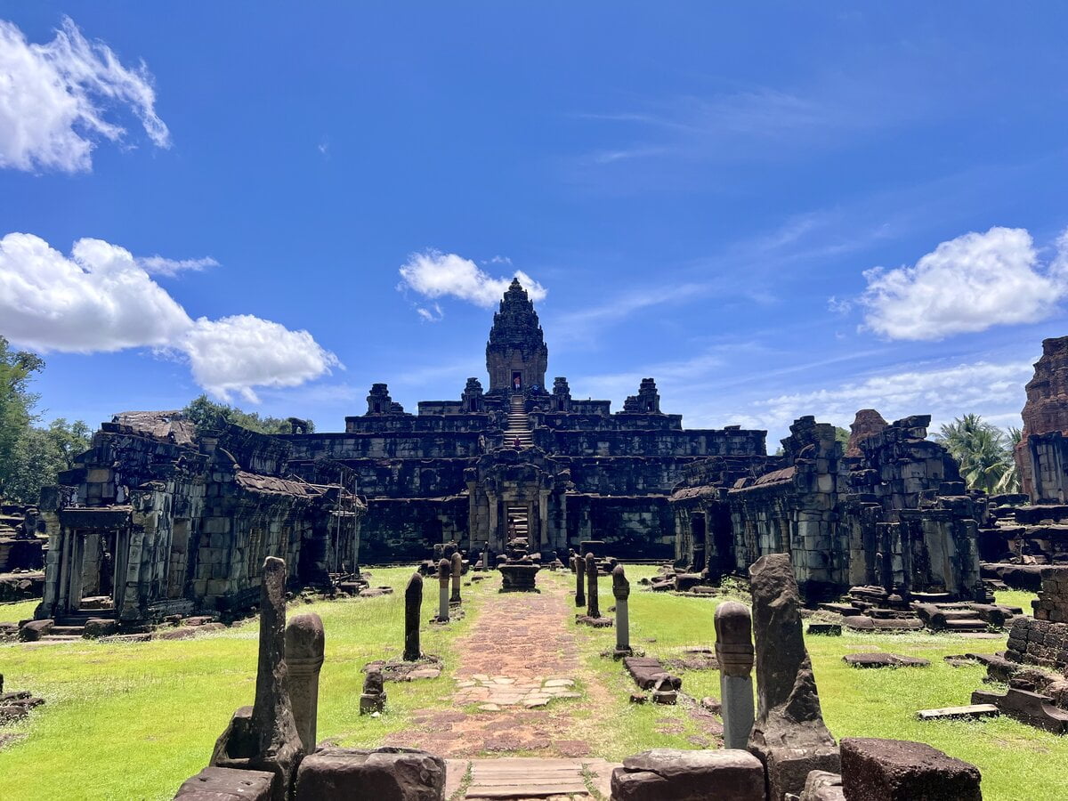 Front view of Bakong Temple in Cambodia showing the central pyramid sanctuary, ancient stone causeway, ruined galleries, and bright blue sky above the Khmer temple complex near Siem Reap.