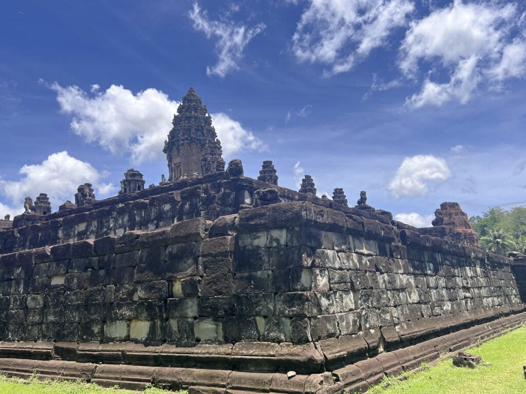 Massive laterite terrace walls of Bakong temple in Cambodia rising toward the central sandstone sanctuary tower under a bright blue sky