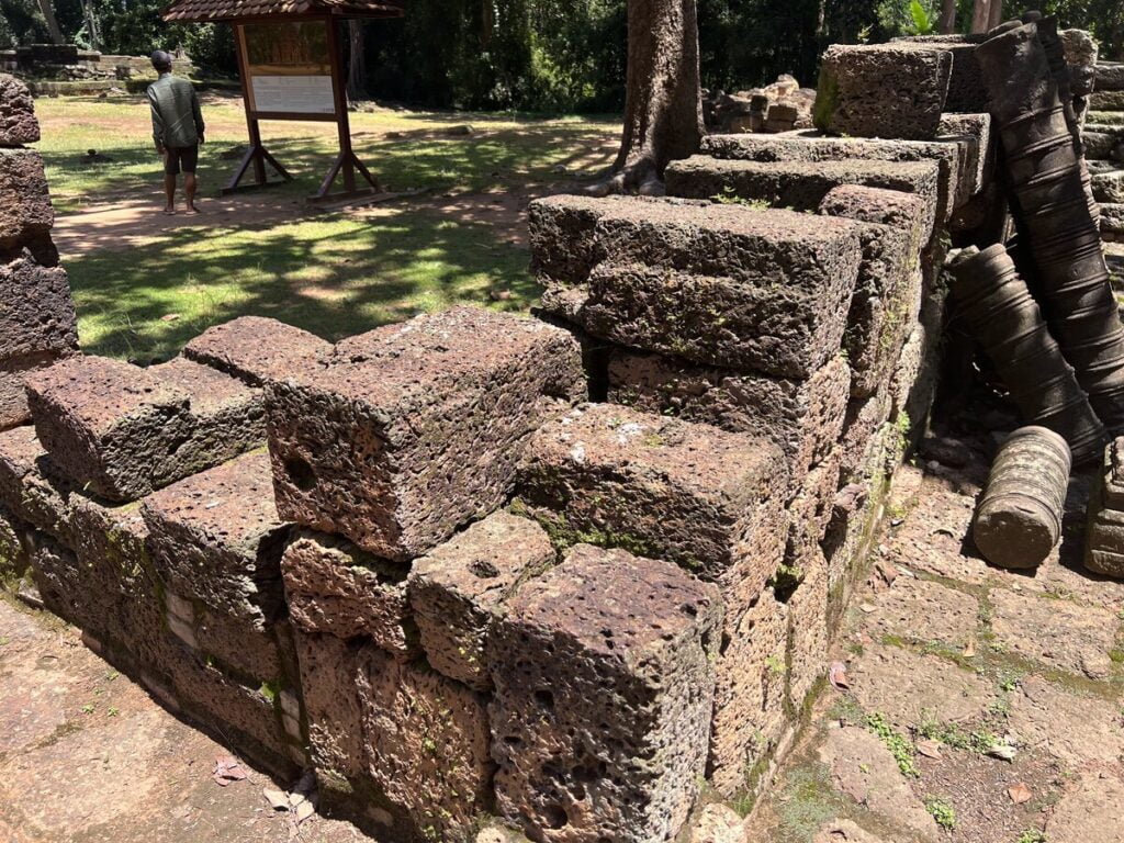 Weathered laterite blocks and collapsed stone ruins at Bakong temple in Cambodia showing the porous volcanic stone construction used in early Khmer architecture
