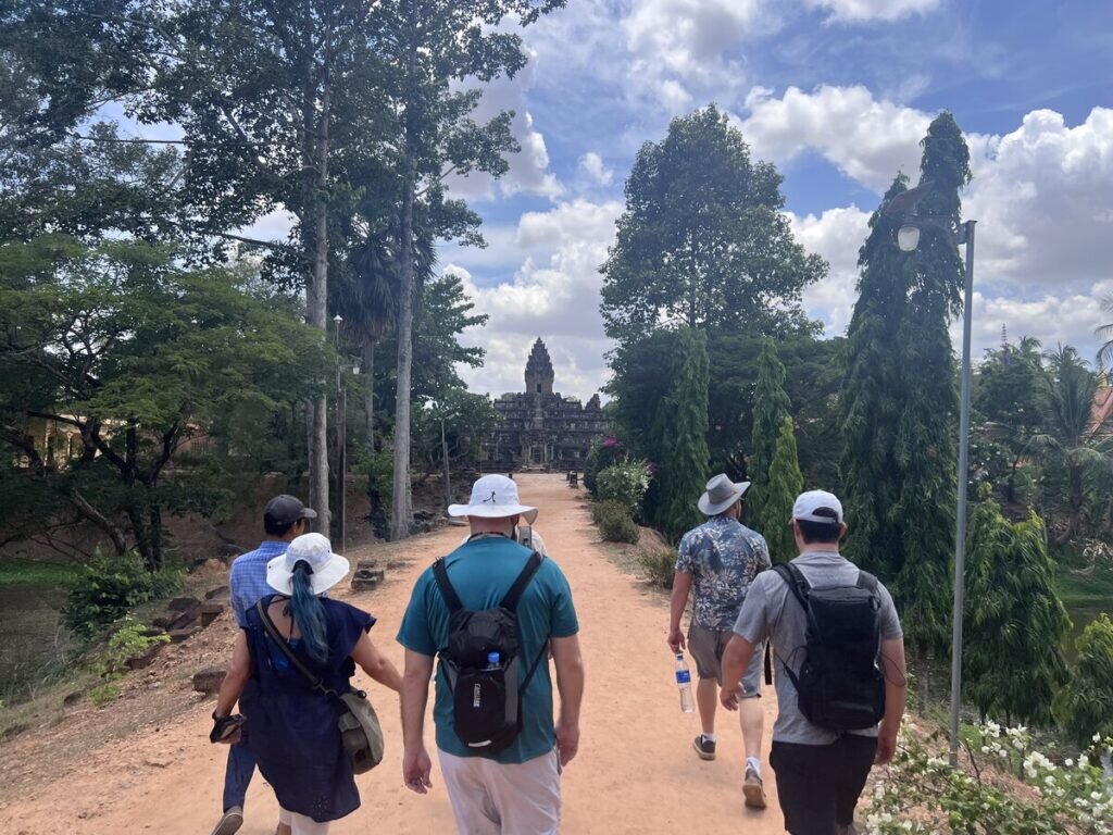 Visitors walking along the main causeway toward Bakong temple in Cambodia surrounded by trees and the ancient Khmer pyramid temple ahead
