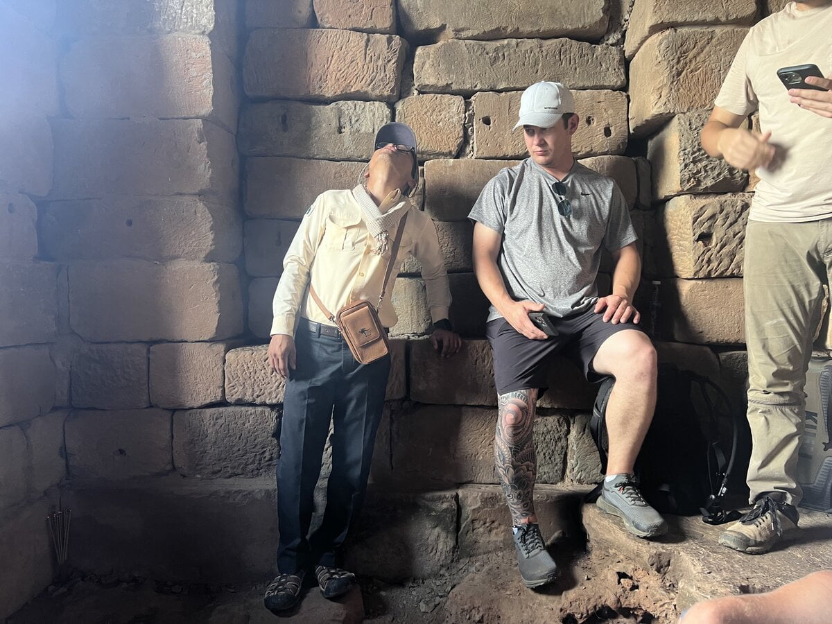 Visitors standing inside the stone central chamber of Bakong temple in Cambodia beneath massive sandstone blocks during the zenith sun alignment event