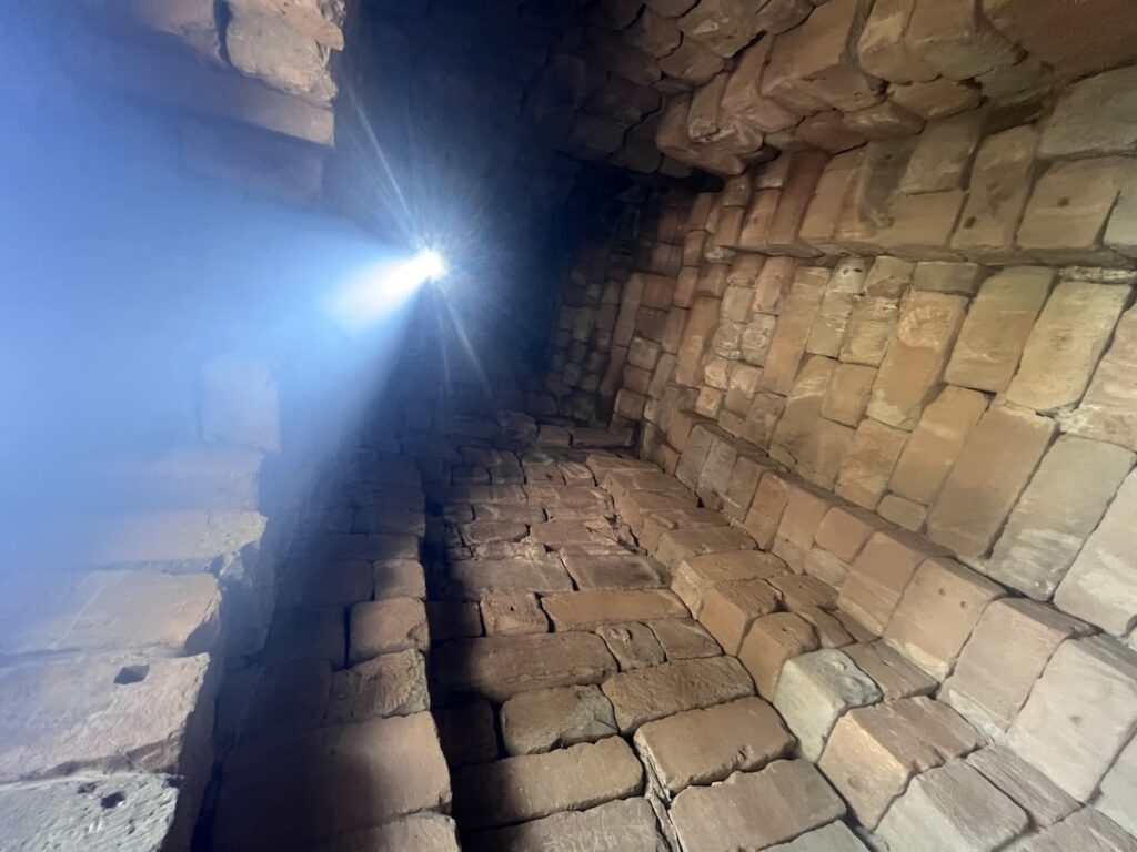 Looking upward inside the Bakong temple sanctuary in Cambodia as sunlight enters through the roof opening and illuminates the massive sandstone interior during the zenith sun event