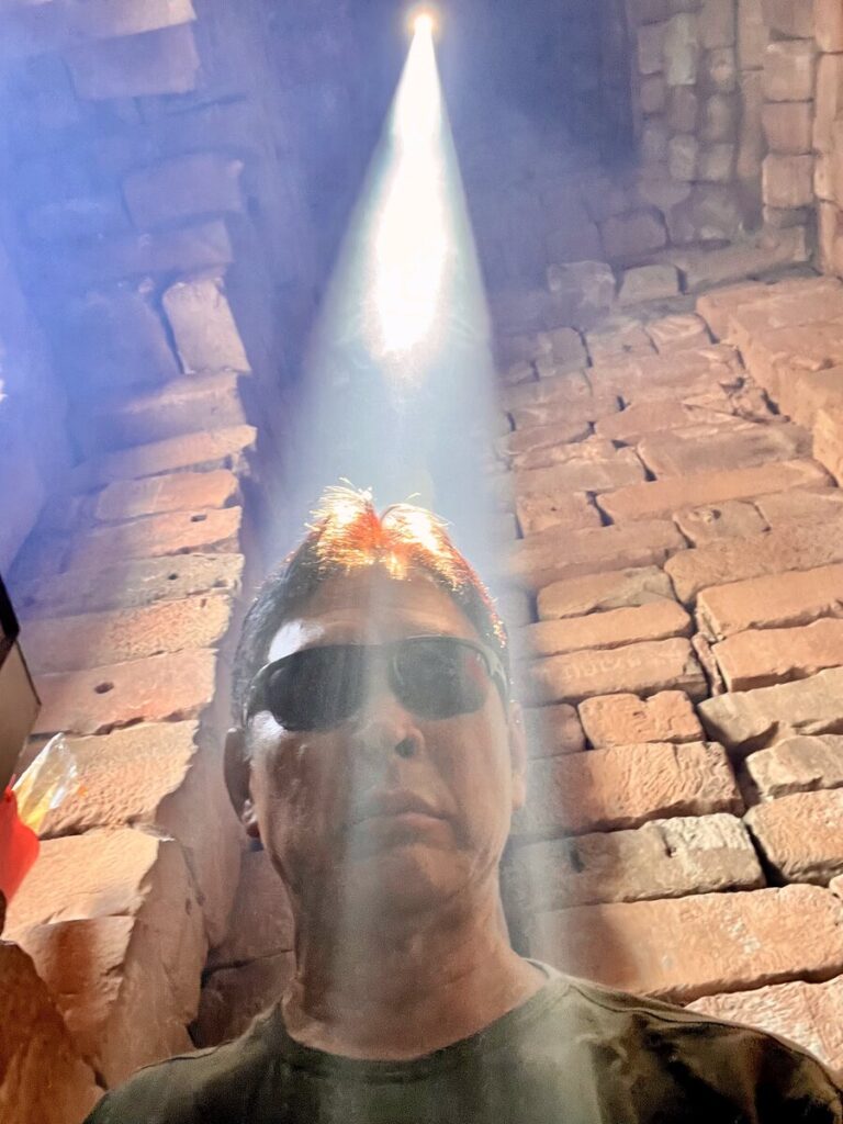 Visitor standing beneath the vertical zenith sun beam inside the central sanctuary tower of Bakong temple in Cambodia during the solar alignment event