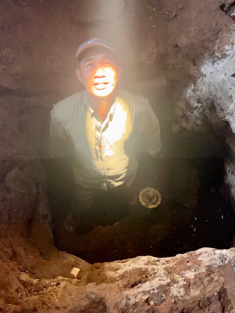Local guide standing inside the dark central chamber of Bakong temple in Cambodia illuminated by the vertical zenith sun beam entering through the roof opening
