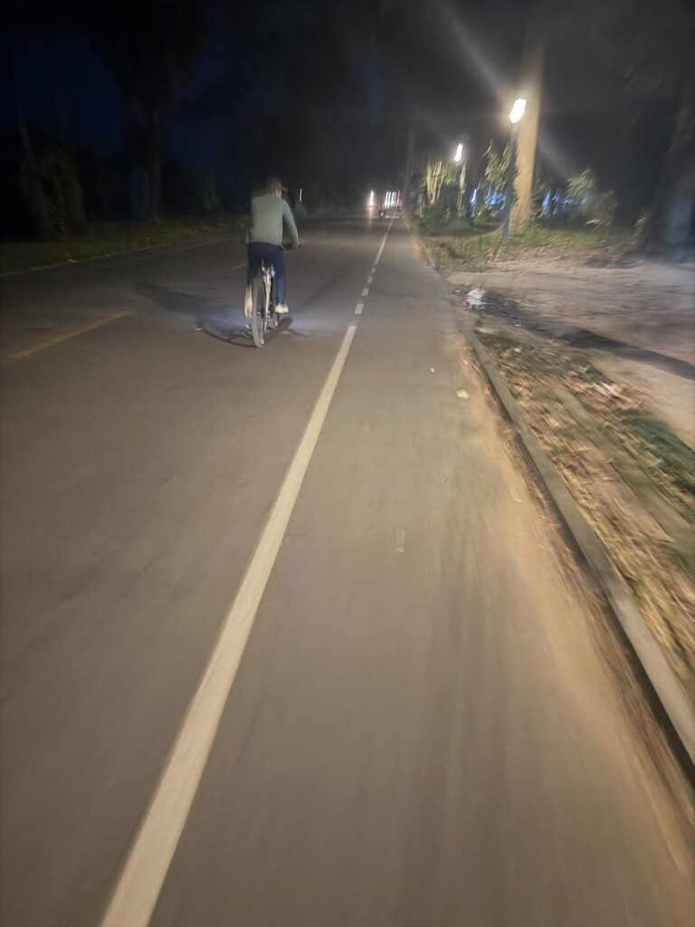 Guide Kanha Phum cycling ahead on a streetlit road near Angkor Wat after dark