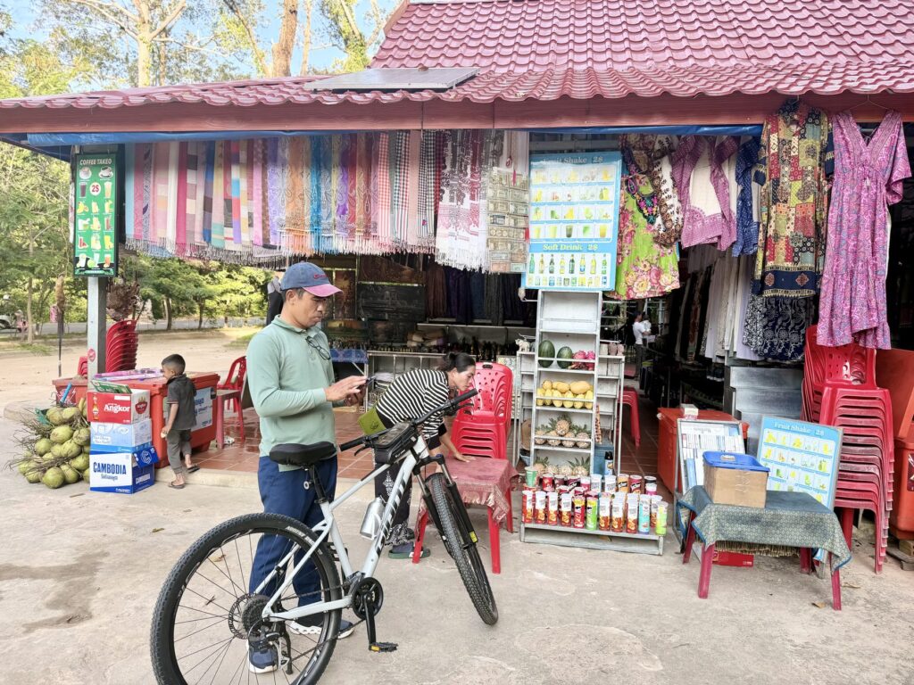 Guide Kanha Phum with a bicycle at a roadside stall selling coconuts and drinks near Ta Keo