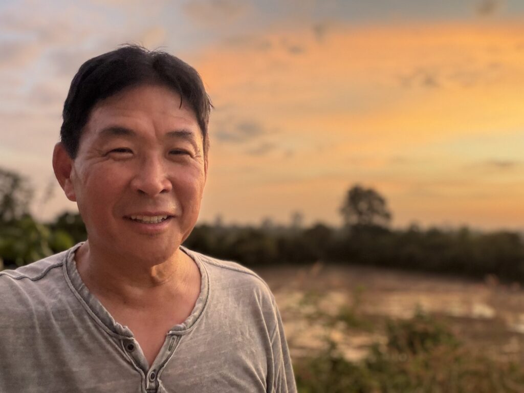 The author smiling in front of an orange sunset sky on the Angkor Thom wall