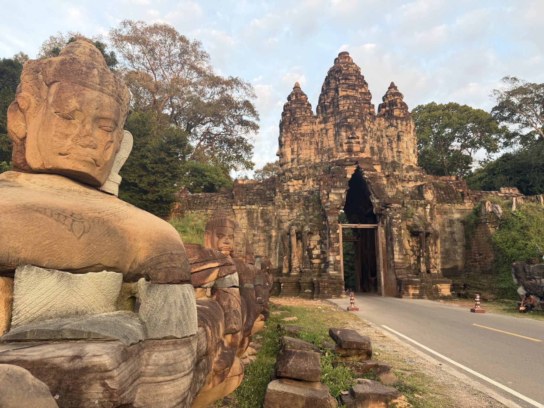 The West Gate of Angkor Thom lit gold by the setting sun with a carved guardian head on the causeway