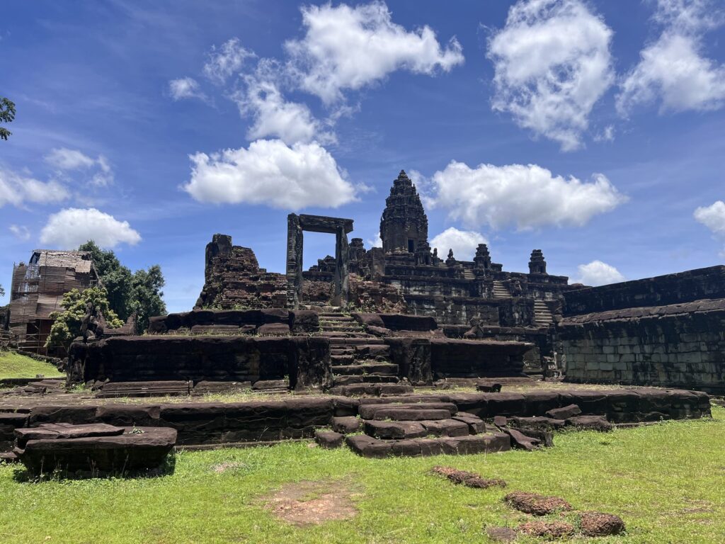 Bakong temple seen across the green lawn of the outer enclosure, with ruined gopura and the central tower