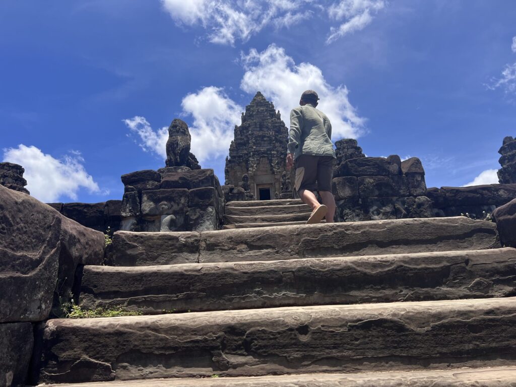 Guide Kanha Phum climbing the steep stone stairs toward Bakong's central tower