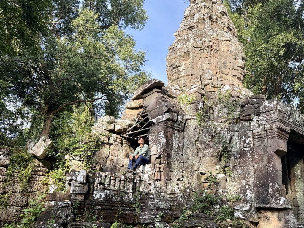 Guide Kanha Phum sitting in a collapsed window of the Banteay Kdei face-tower gate