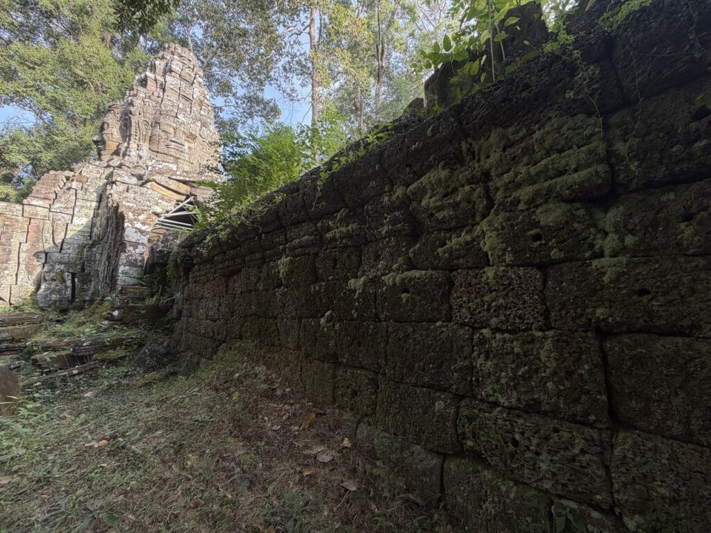 A moss-covered laterite enclosure wall beside the Banteay Kdei south gate tower