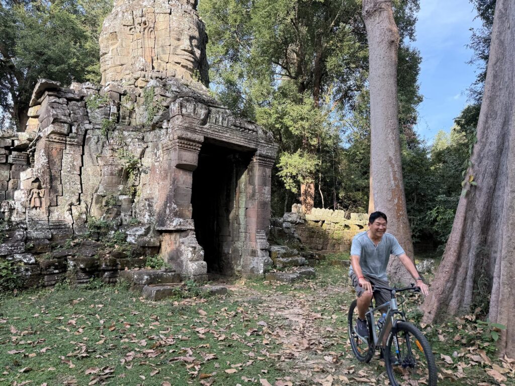 The author riding a mountain bike out of the face-tower south gate of Banteay Kdei