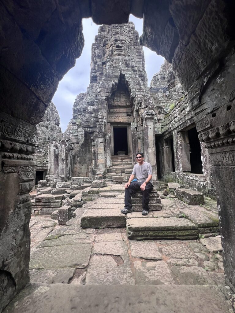 The author sitting on the stone steps, framed by a dark doorway at the Bayon