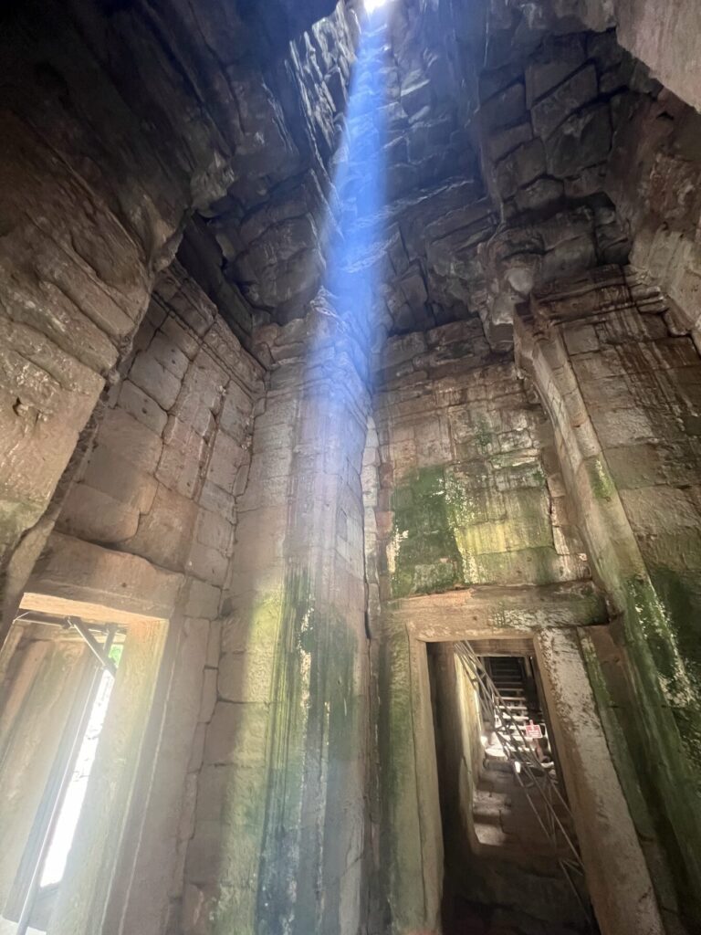 A bright blue zenith beam made visible by incense smoke inside a Bayon tower in August