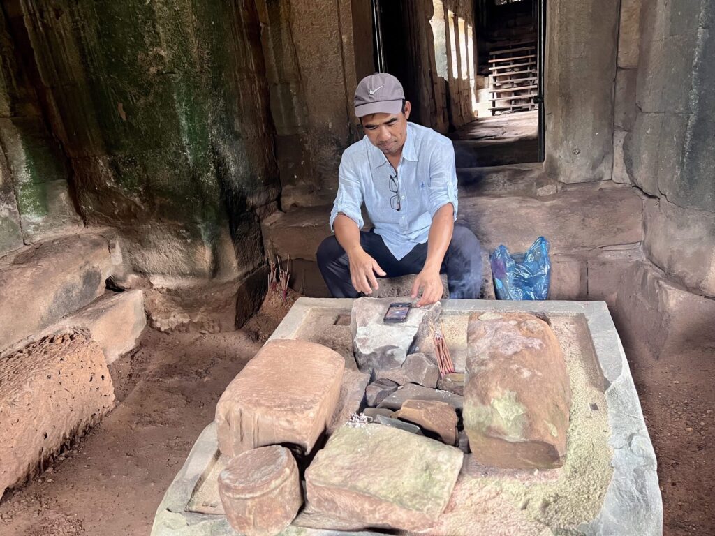 Guide Kanha arranging incense at a stone altar during the zenith passage at the Bayon