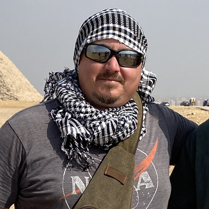 Ben van Kerkwyk of UnchartedX in sunglasses and a keffiyeh on the Giza plateau with a pyramid behind him