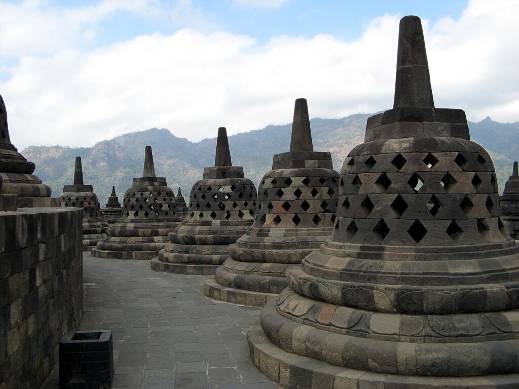 Sunrise over the upper terraces of Borobudur in Java, Indonesia, with rows of bell-shaped stone stupas silhouetted against the morning sky.