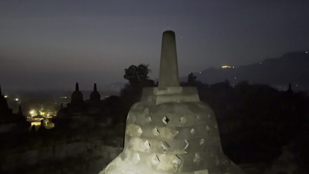 Silhouette of a stupa with village lights in the valley below during blue hour