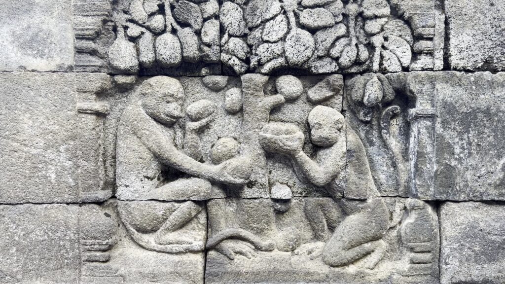 Carved relief panel with seated figures and animals on a gallery wall at Borobudur