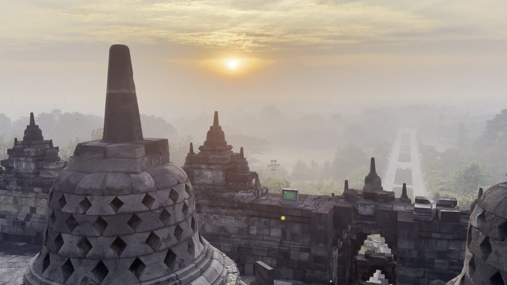 The sun rising behind a latticed stupa at Borobudur with mist in the valley