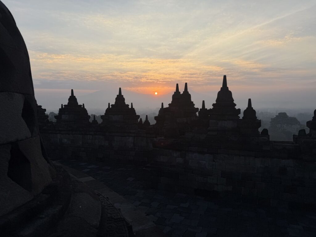 Silhouetted terraces of Borobudur under an orange sunrise sky
