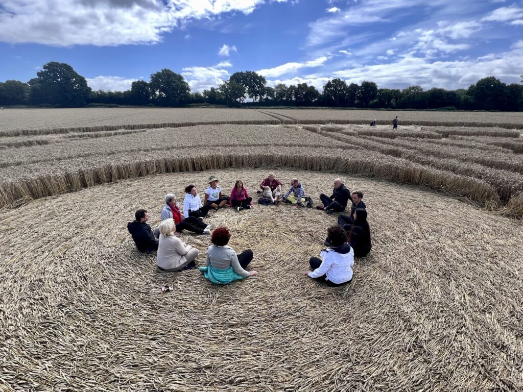 The tour group sitting in a circle in the middle of an English crop circle