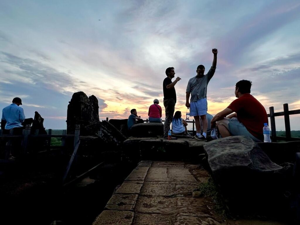 Tour members silhouetted against the sunrise on top of the Koh Ker pyramid, one with a raised fist