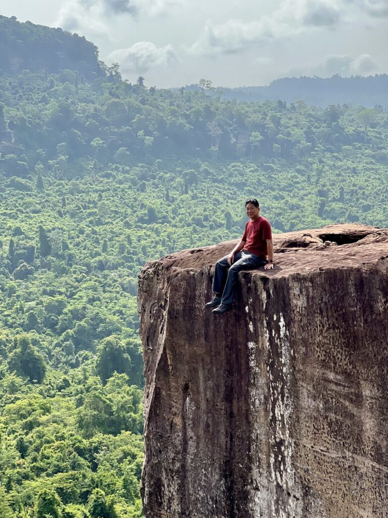 The author sitting on the edge of a sheer rock pillar at the Amazing Cliff on Phnom Kulen