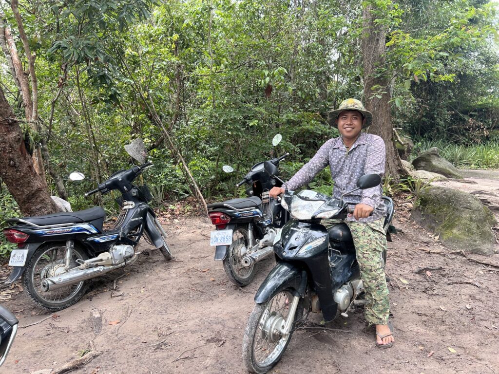 The camp leader smiling on his motorbike, with a second bike parked beside him