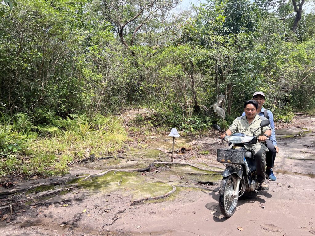 Kanha riding on the back of a motorbike across a flat rock trail on Phnom Kulen