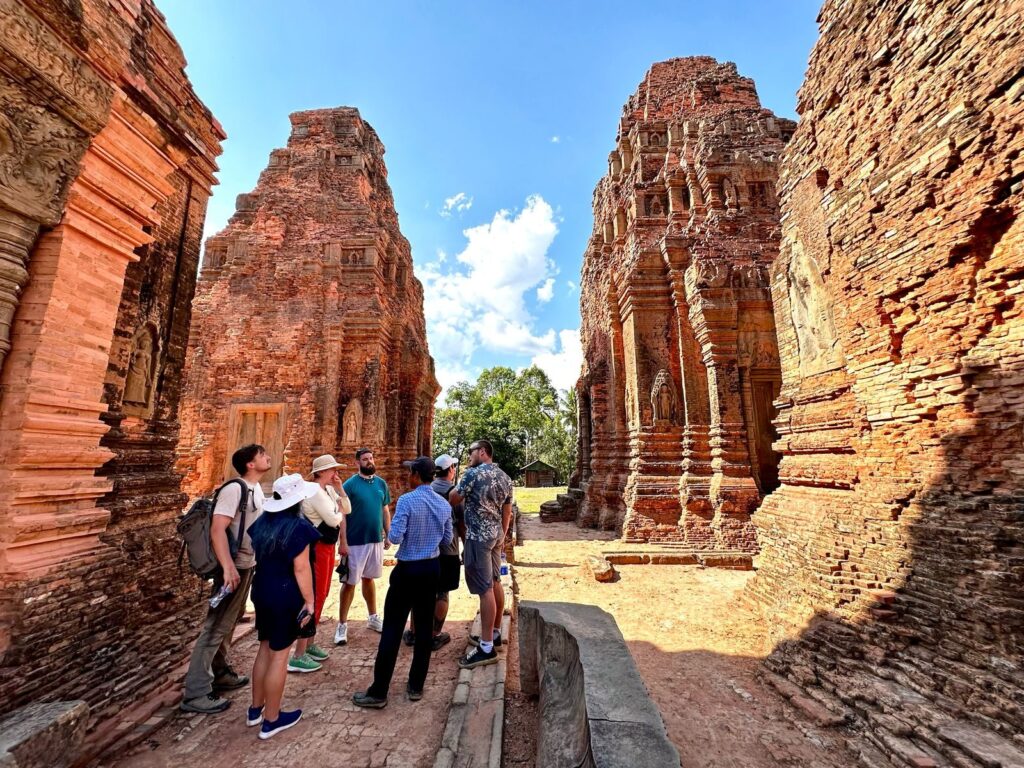 The April 2025 tour group walking between two brick towers at Lolei