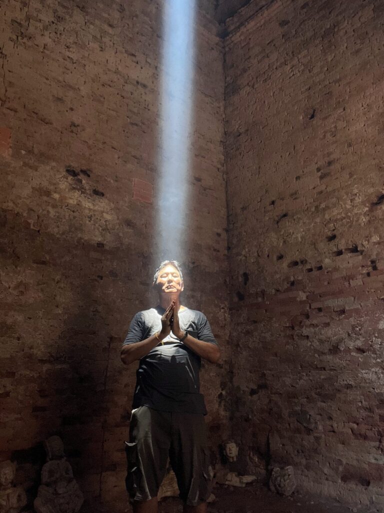 The author standing in the zenith sunbeam inside a Lolei tower, hands pressed together