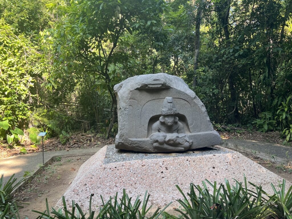 A carved Olmec altar with a seated figure emerging from a niche, among the trees at La Venta Park in Villahermosa