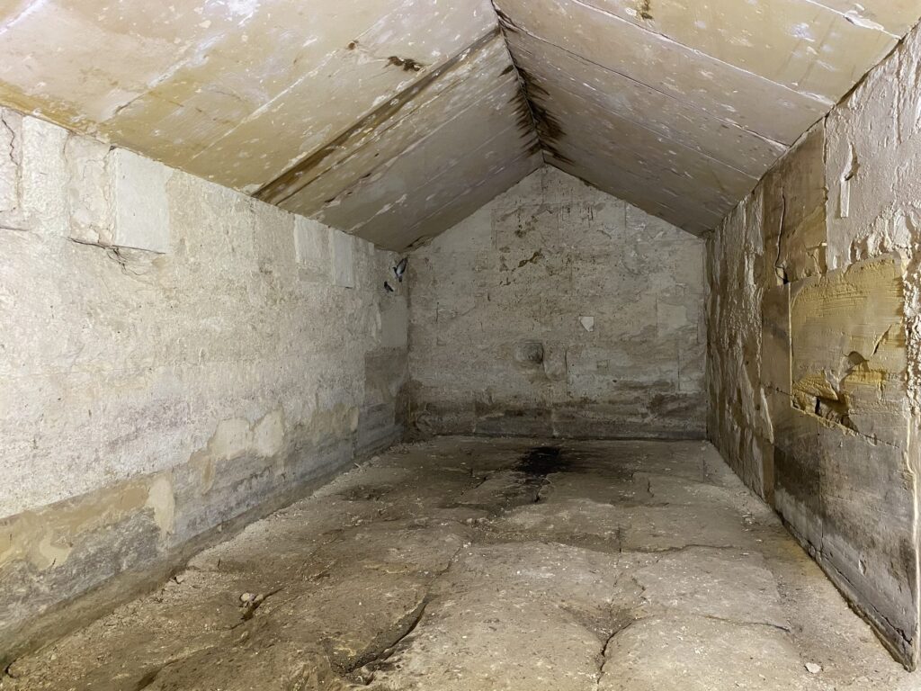 Inside an Osirion chamber with a pitched stone roof and plain undecorated walls