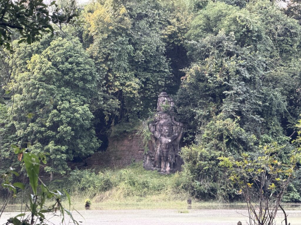 A carved garuda figure on the laterite outer wall of Preah Khan across a lily-covered moat