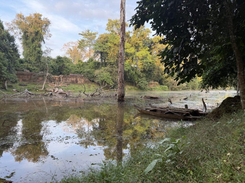 A wooden boat in the moat at Preah Khan with ruins and trees reflected in the water